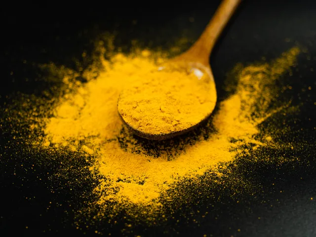 Bright golden-yellow turmeric powder on a wooden spoon against a black background